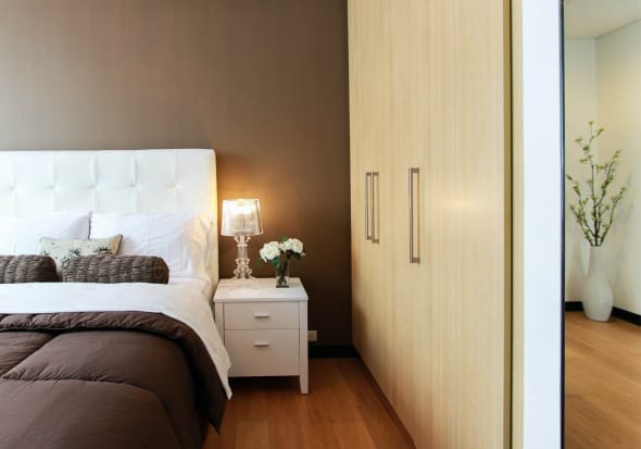 Elegant bedroom with white bed, dark brown accent wall, and natural wood wardrobe.