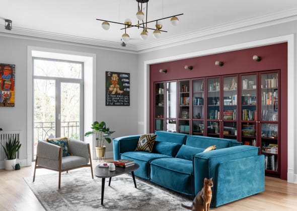 Eclectic living room with blue velvet sectional sofa and burgundy bookshelf backdrop.