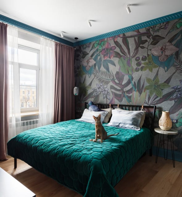 Boho-style bedroom with botanical wallpaper and teal velvet bedspread under daylight.