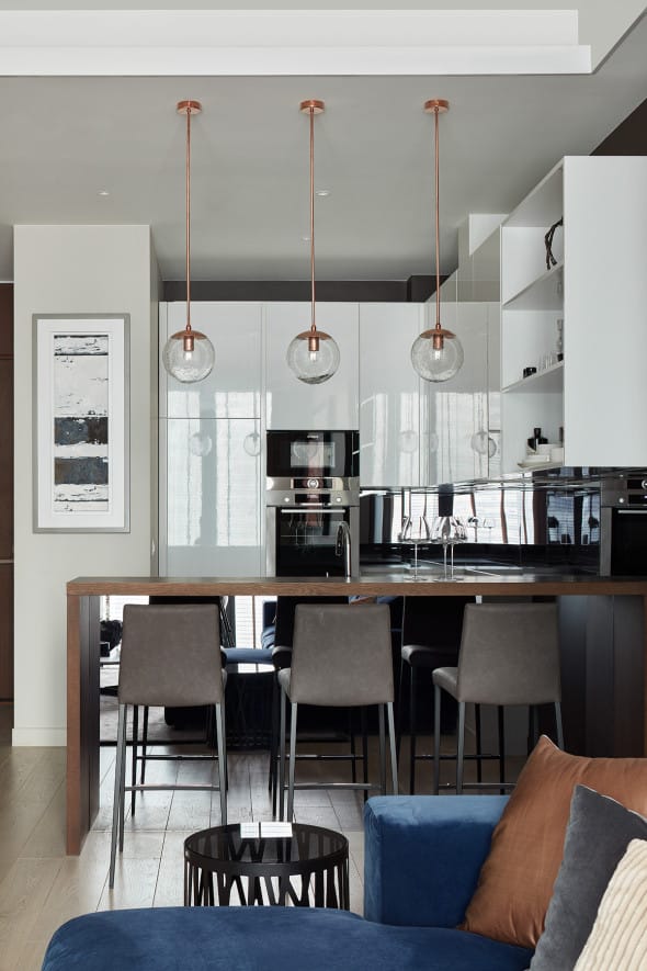 Contemporary kitchen with glossy white cabinets, built-in appliances, a wooden breakfast bar, and three hanging pendant lights.